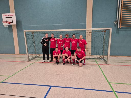 Die Fußballmannschaft in roten Trikots steht vor einem Tor in einer Sporthalle.